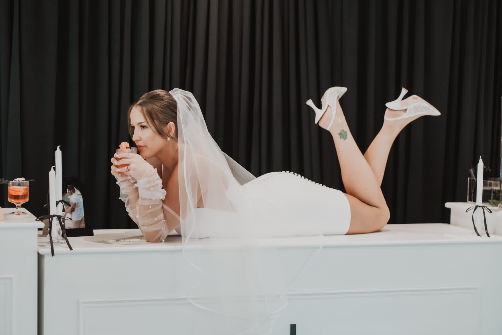 Bride reclining at the reception bar with her veil cascading behind her, long-wear bridal makeup intact