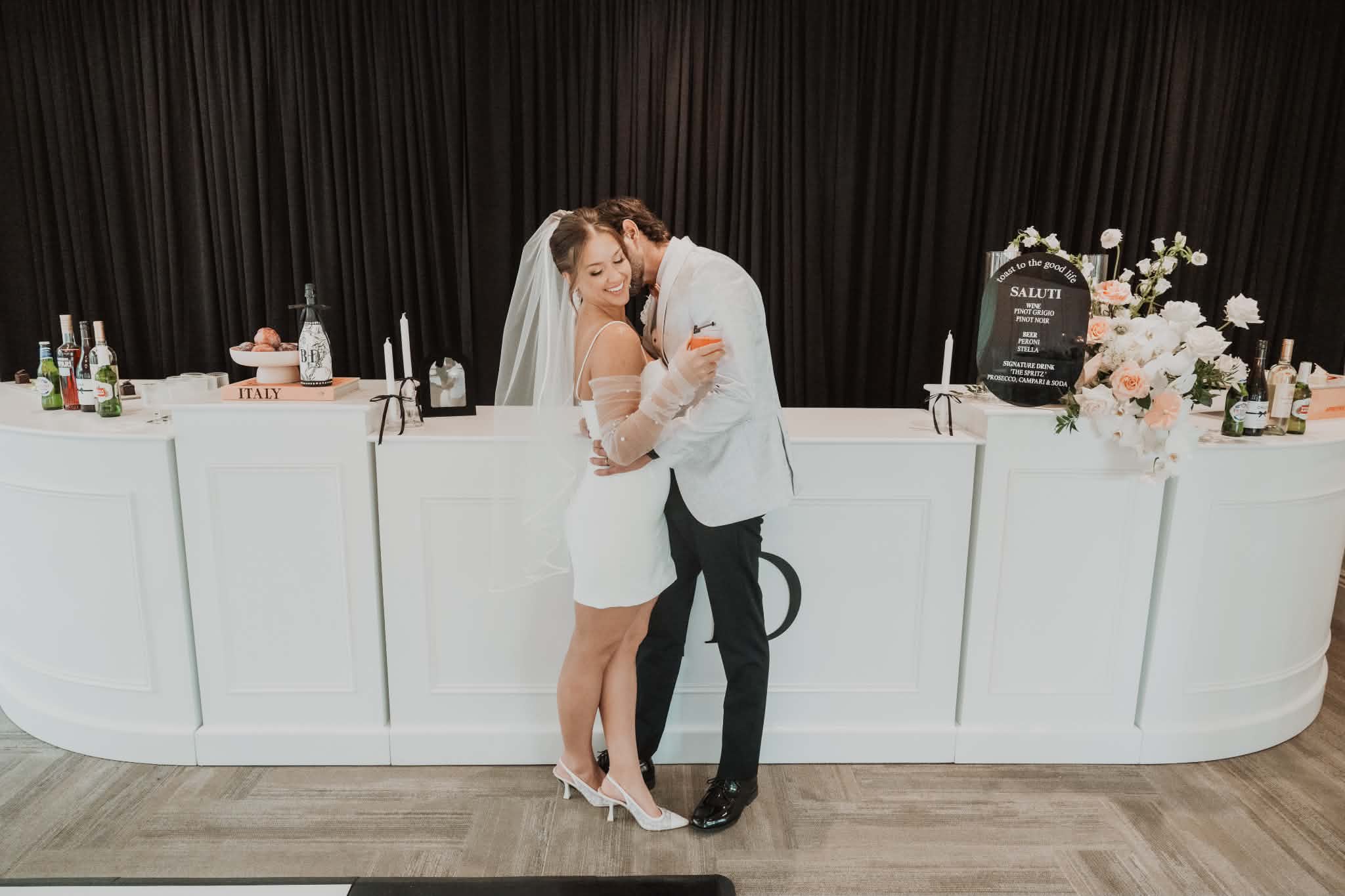 Bride and groom embracing at their reception bar, her wedding-day beauty look intact