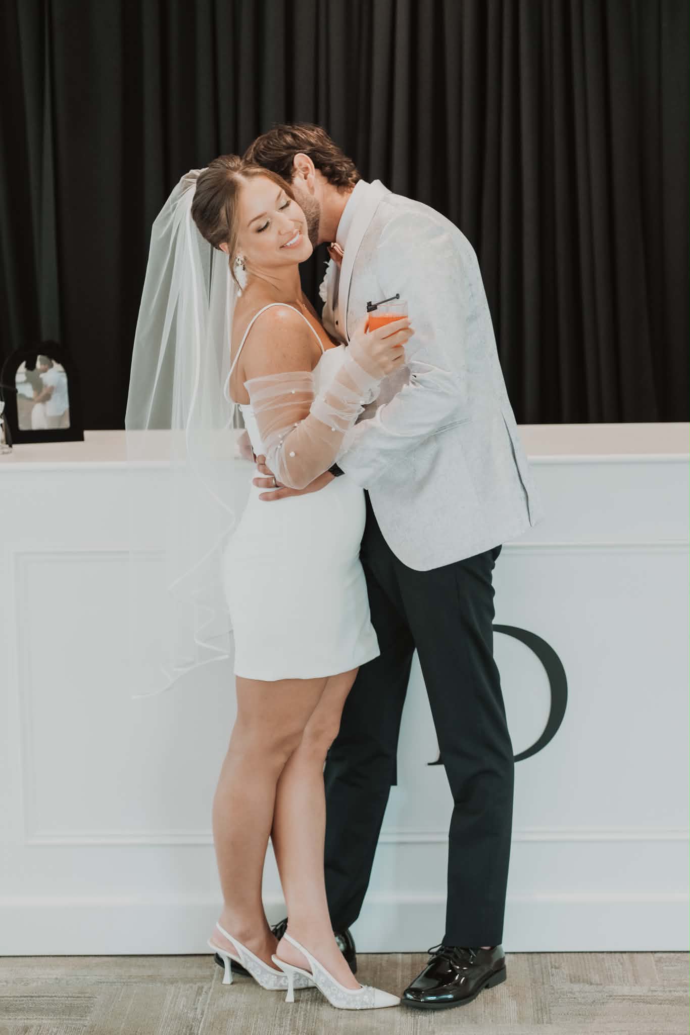 Groom kissing the bride's cheek at the reception, her wedding-day hair and makeup still fresh