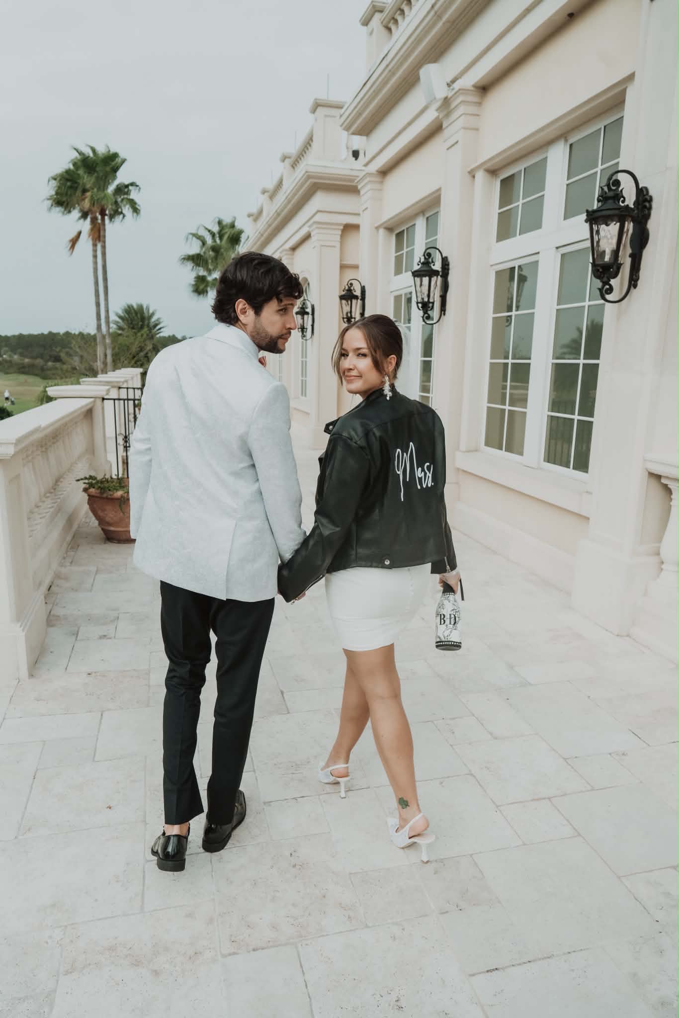 Bride in a monogrammed 'Mrs.' jacket walking with her groom after the reception